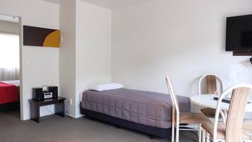 A bedroom with a bed, a desk with a computer, a chair, a TV mounted on the wall, and a painting on the wall.