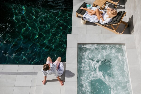 Un área de piscina con agua cristalina, un jacuzzi y sillones de descanso.