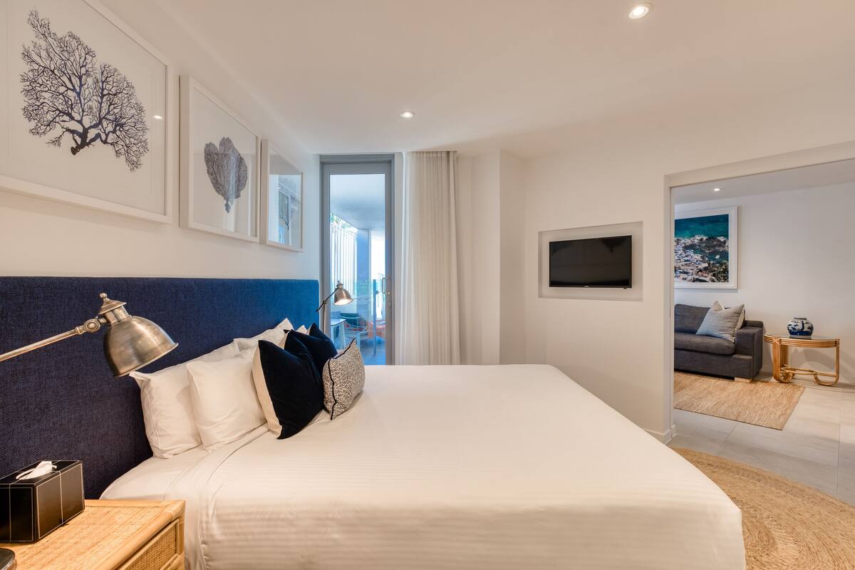 A modern hotel room with a large bed, a desk with a lamp, a television, and artwork on the walls.