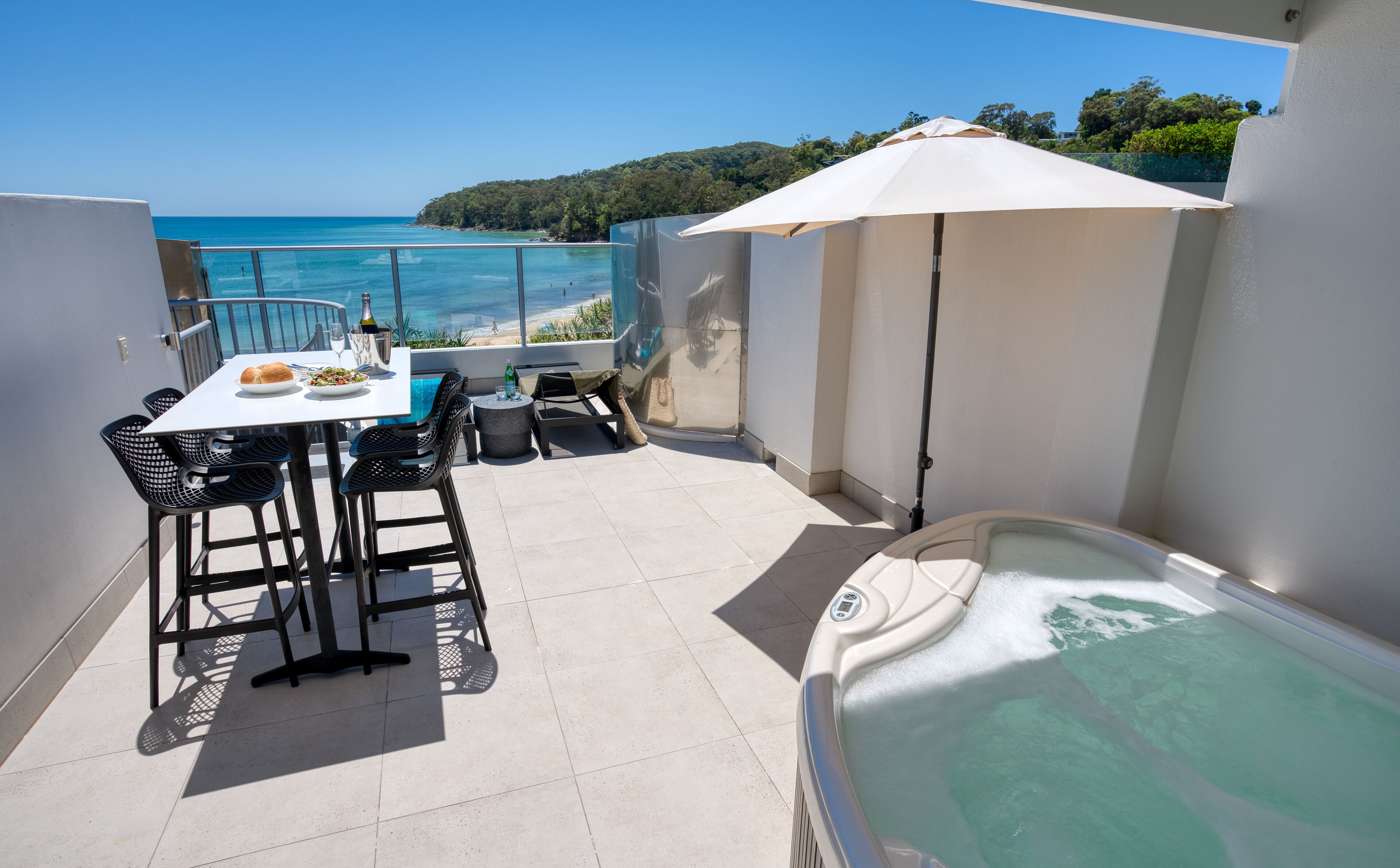 A balcony with a table set for dining, a hot tub, and a view of the ocean.