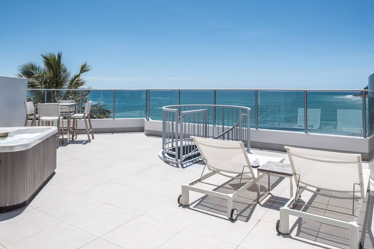 A balcony with a hot tub, lounge chairs, and a view of the ocean.