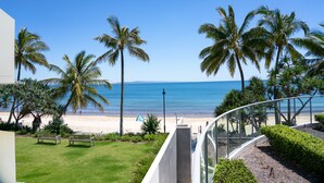Un balcon avec vue sur une plage, des palmiers et un ciel bleu dégagé.