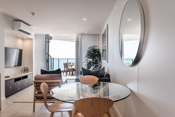 A modern living room with a glass-top dining table, a sofa, and a TV.
