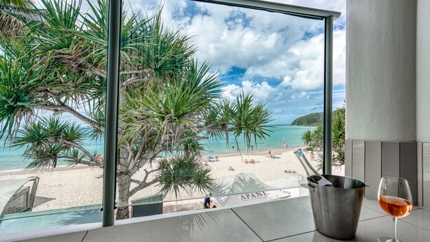 Un balcon donnant sur une plage, un verre de vin et un seau en métal.