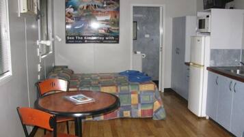 A compact room with a bed, a small table, a chair, a kitchenette, and a poster on the wall.