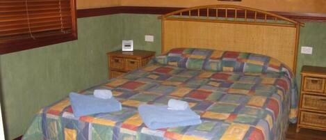 Un dormitorio con cabecera de cama de madera, colcha colorida, dos mesitas de noche y una mesilla.