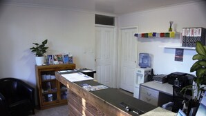 A reception area with a wooden reception desk, a potted plant, a water dispenser, and a shelf with various items.