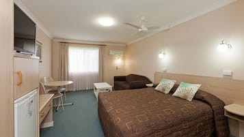 A hotel room with a bed, a desk, a chair, a television, and a ceiling fan.
