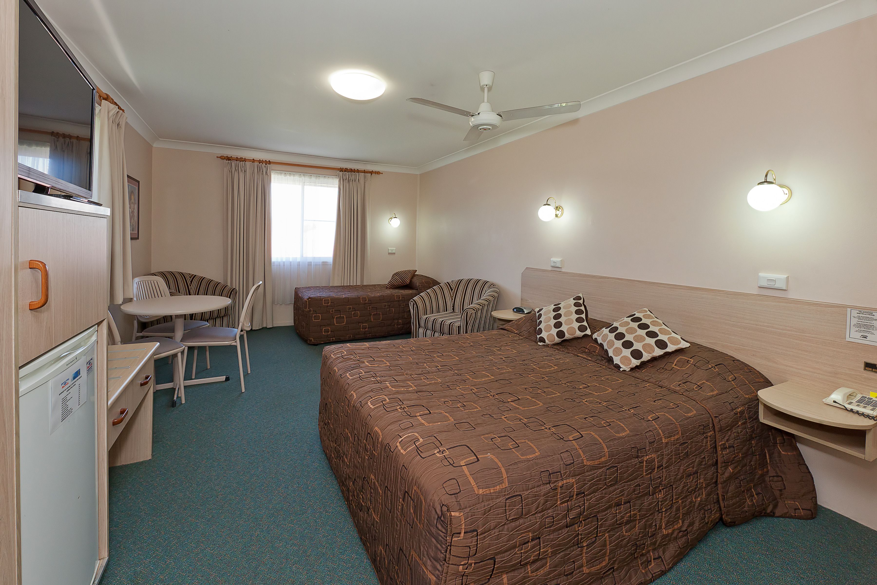 Habitación de hotel con una cama, un escritorio con teléfono, una silla, una mesita y un ventilador de techo.