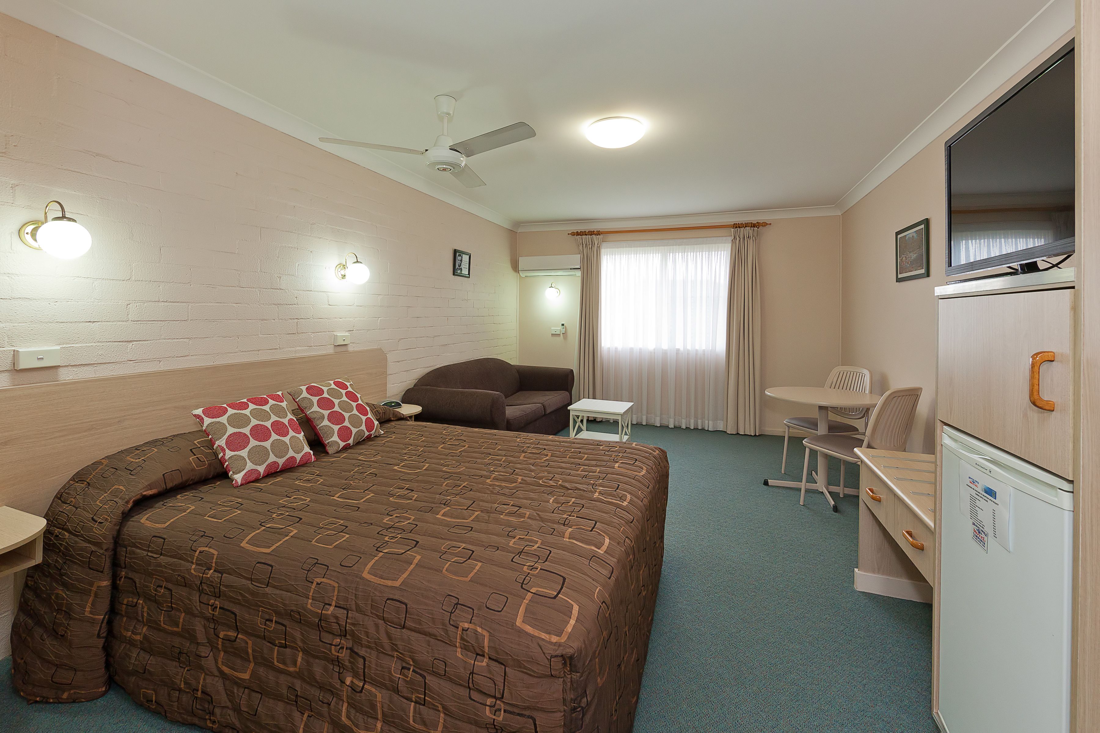 Una habitación de hotel con una cama, un escritorio, una silla, un ventilador de techo y un televisor.