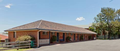 A single-story motel with a tiled roof, a covered parking area, and a small front garden.