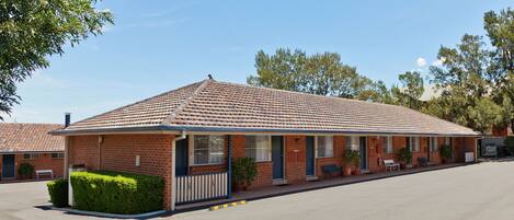 A motel with a tiled roof, brick walls, and a covered parking area.