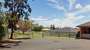 A parking area with a fenced green space, a building with a red roof, and a clear sky. - Abraham Lincoln Motel (East Tamworth)