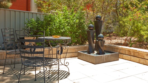 An outdoor patio with a metal table and chairs, a decorative fountain, and a garden with various plants. - Abraham Lincoln Motel (East Tamworth)