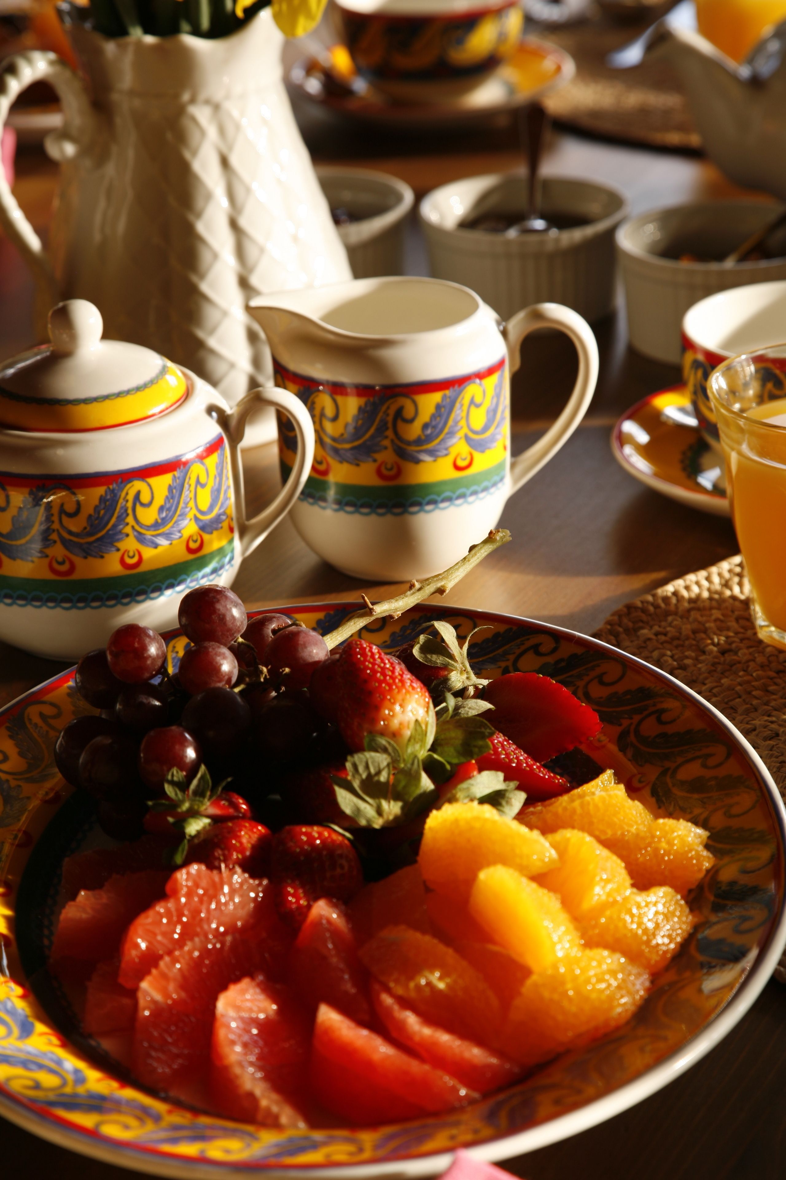 Een tafel met een schaal fruit, theepotten en kopjes.