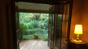 Une porte ouverte donnant sur un jardin où se trouvent une plante en pot et une lampe de table.