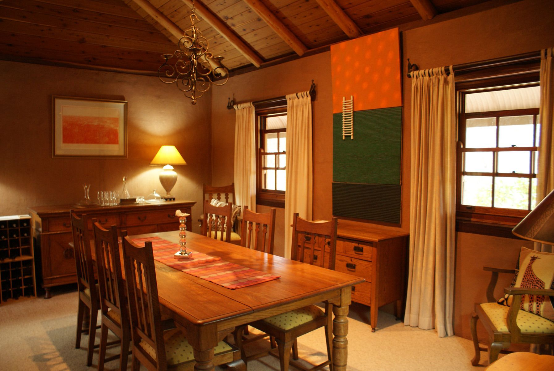 A dining area with a wooden table, chairs, a chandelier, a lamp, and a green accent wall.