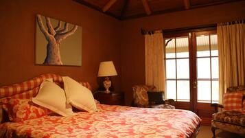 A bedroom with a large bed, a nightstand with a lamp, a chair, and a window with curtains.