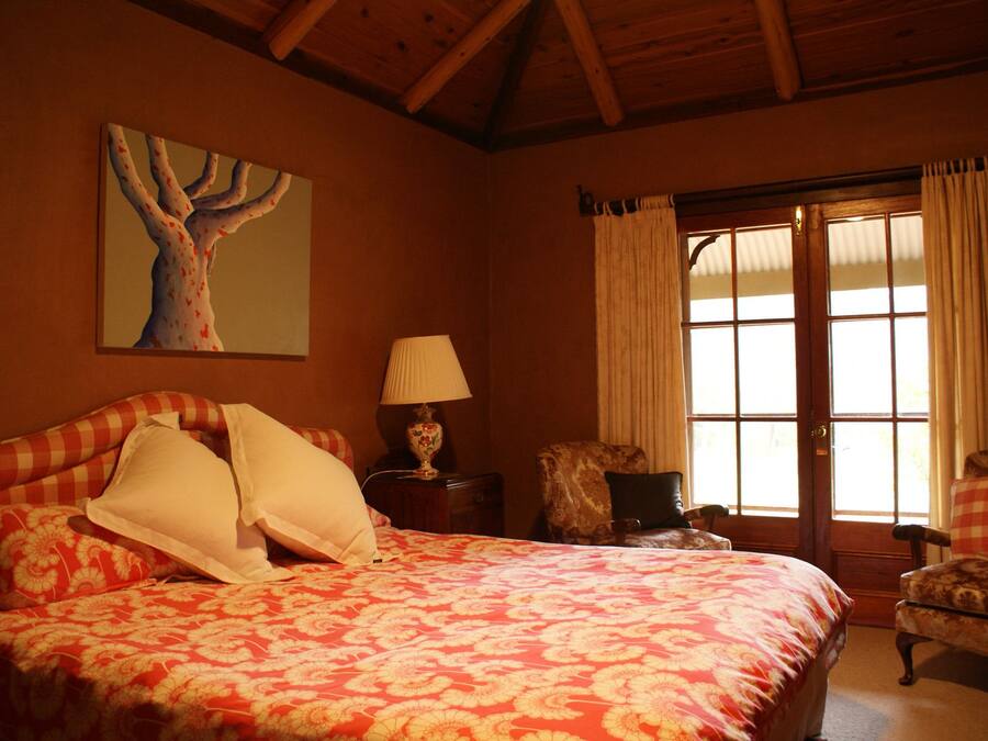 A bedroom with a large bed, a nightstand with a lamp, a chair, and a window with curtains.
