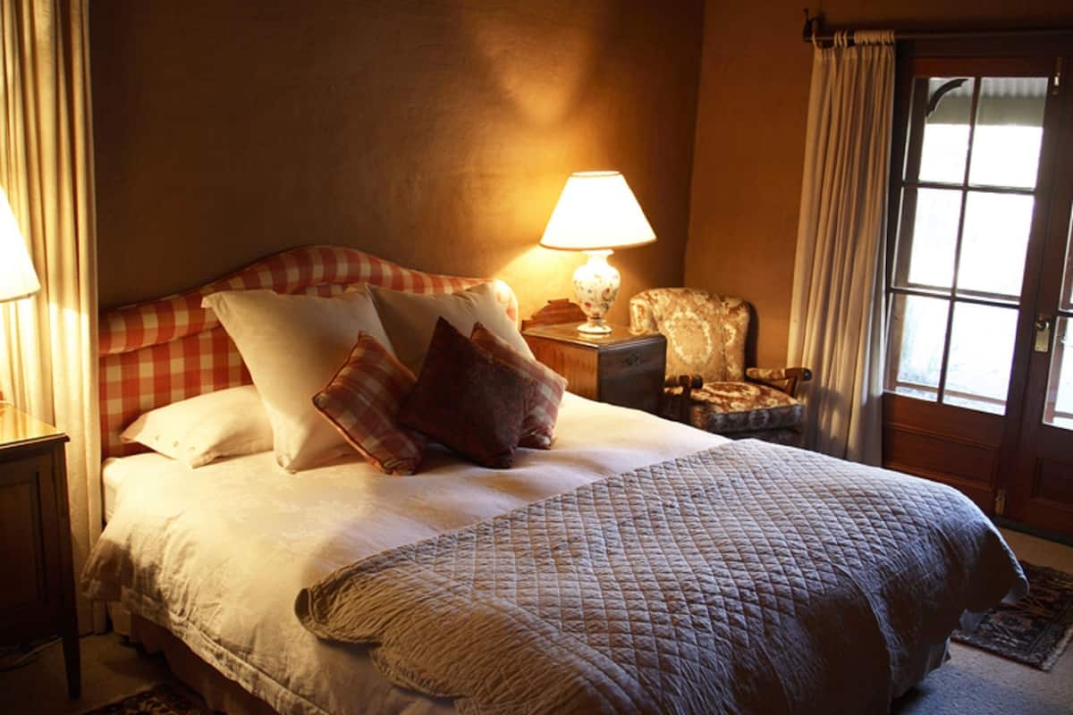 Een goed verlichte slaapkamer met een groot bed, een nachtkastje met een lamp, een stoel en een kamerbreed tapijt met een patroon.