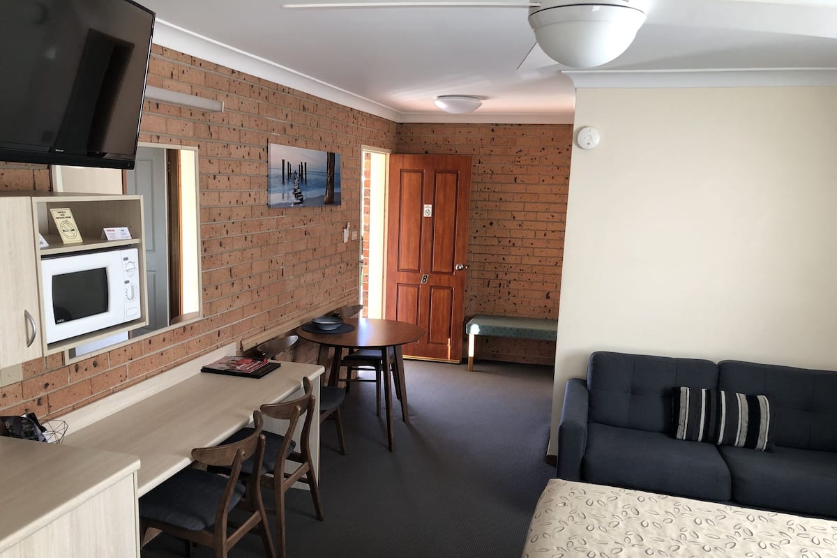 A compact room with a kitchenette, a dining area, and a seating area with a sofa and a bench.