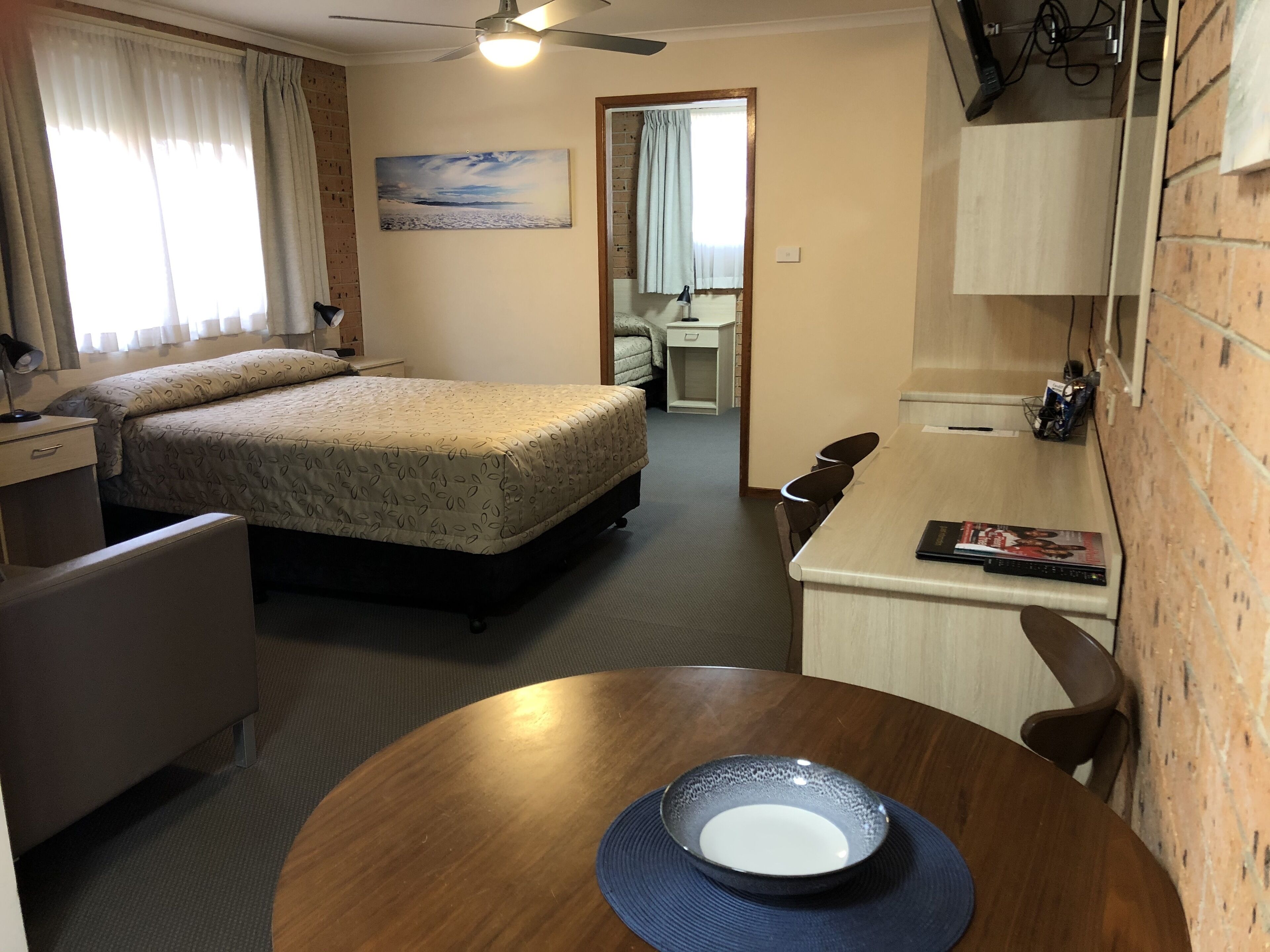 Habitación de hotel con cama, escritorio, silla, mesa con un bol y ventilador de techo.