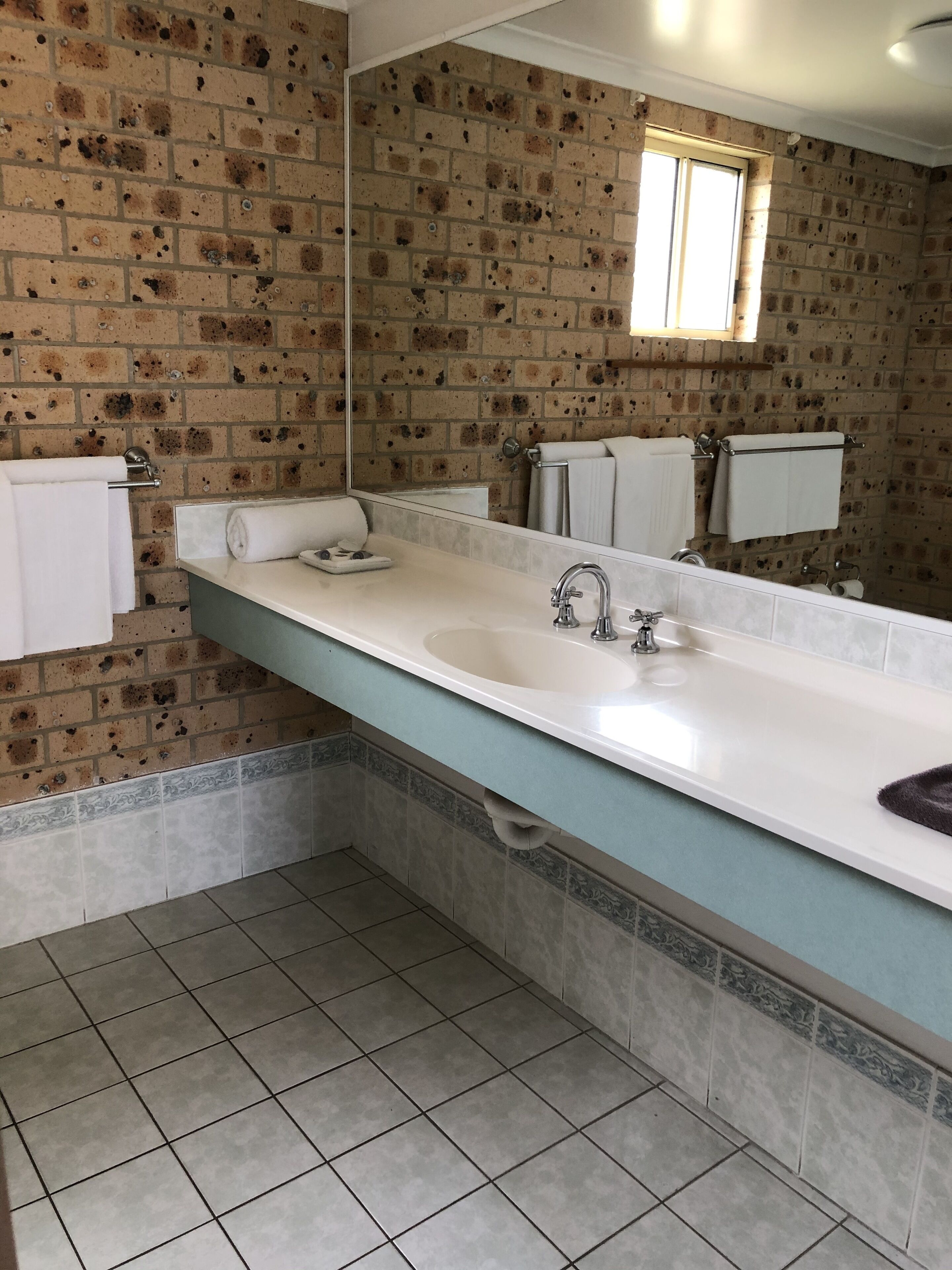 Un baño con un lavamanos blanco, un espejo y una ventana.