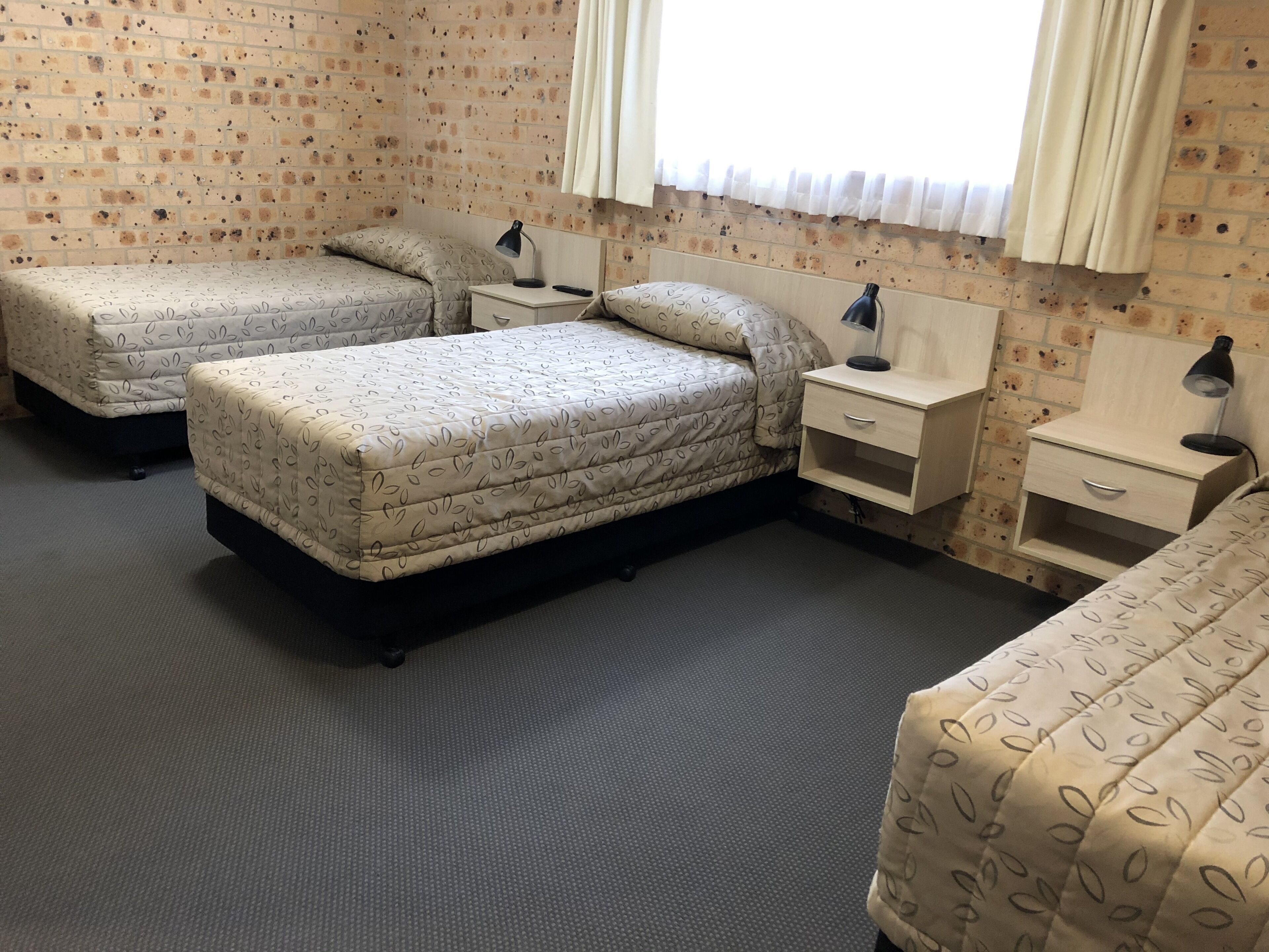 Ein Zimmer mit zwei Betten, jeweils mit einem gemusterten Überwurf, einem Nachttisch mit Lampe und einem Fenster mit Vorhängen.