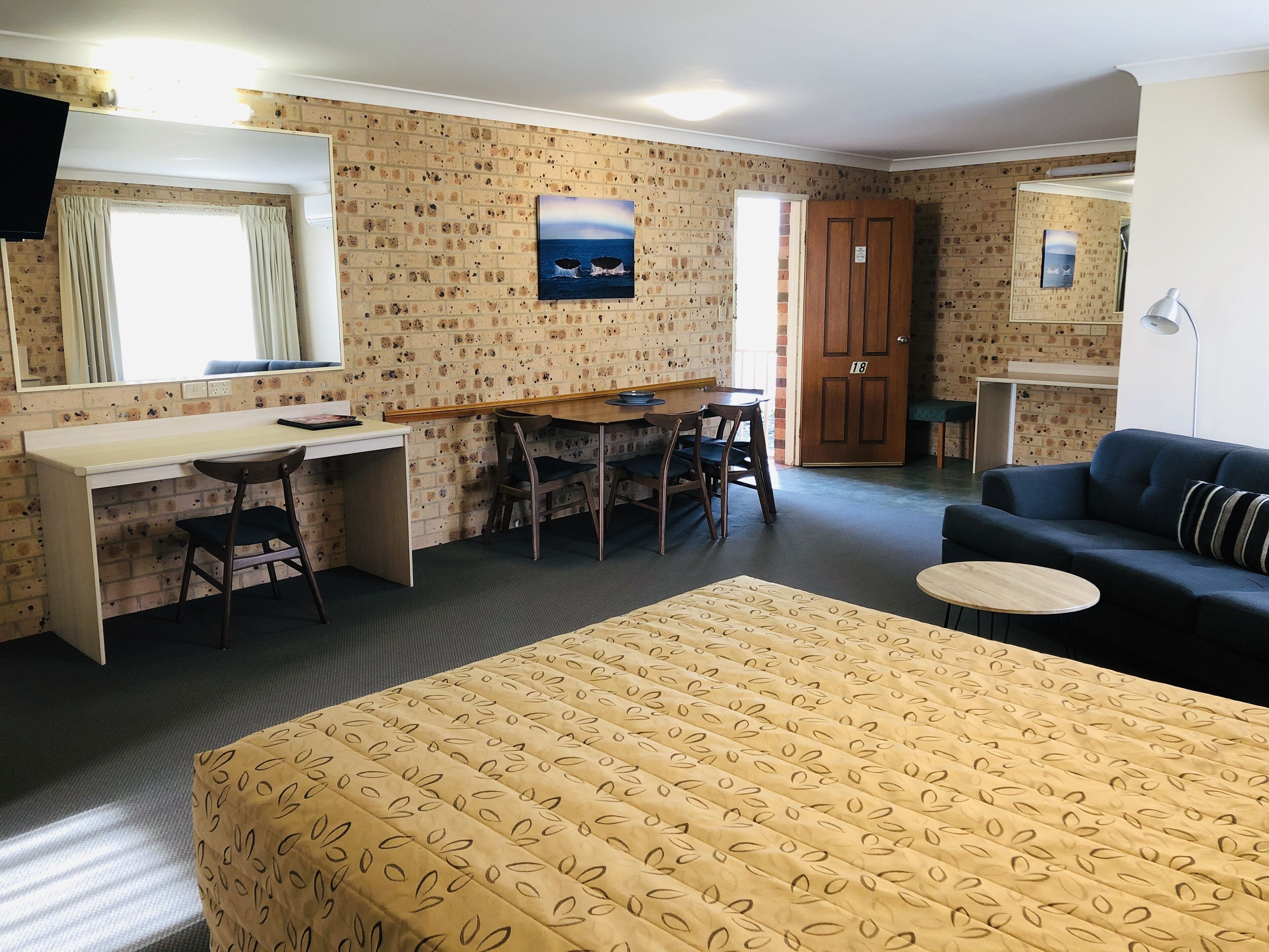 Une chambre d’hôtel comprenant un lit, un bureau, une chaise, un canapé, une petite table, un téléviseur et une porte.
