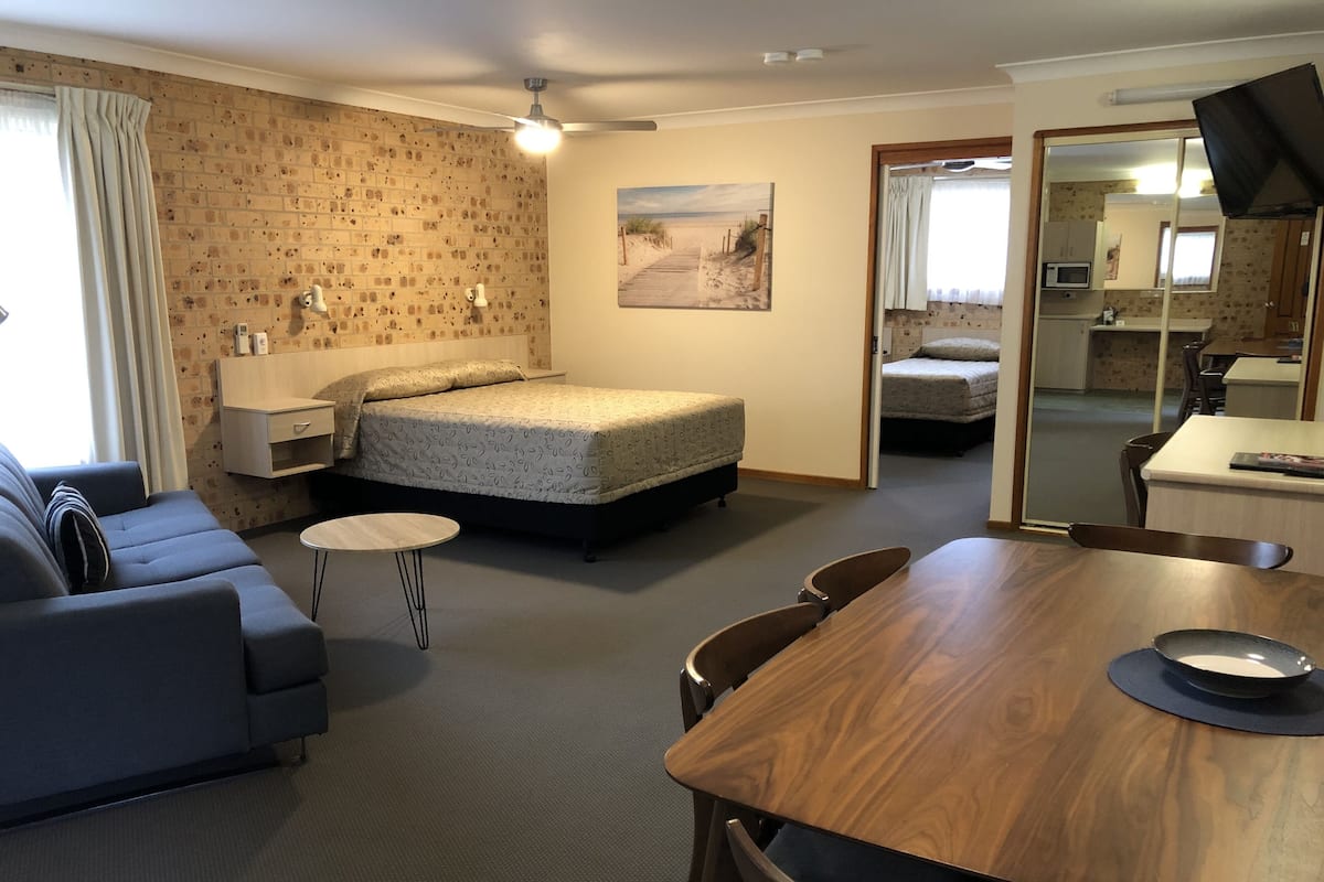 A hotel room with a bed, a sofa, a dining table, and a mirror.