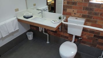 A bathroom with a white toilet, a sink with a mirror, and a brick wall.