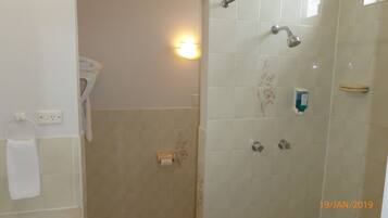 A bathroom with a toilet, a towel rack, a hand dryer, a shower with a handheld showerhead, and a soap dispenser.
