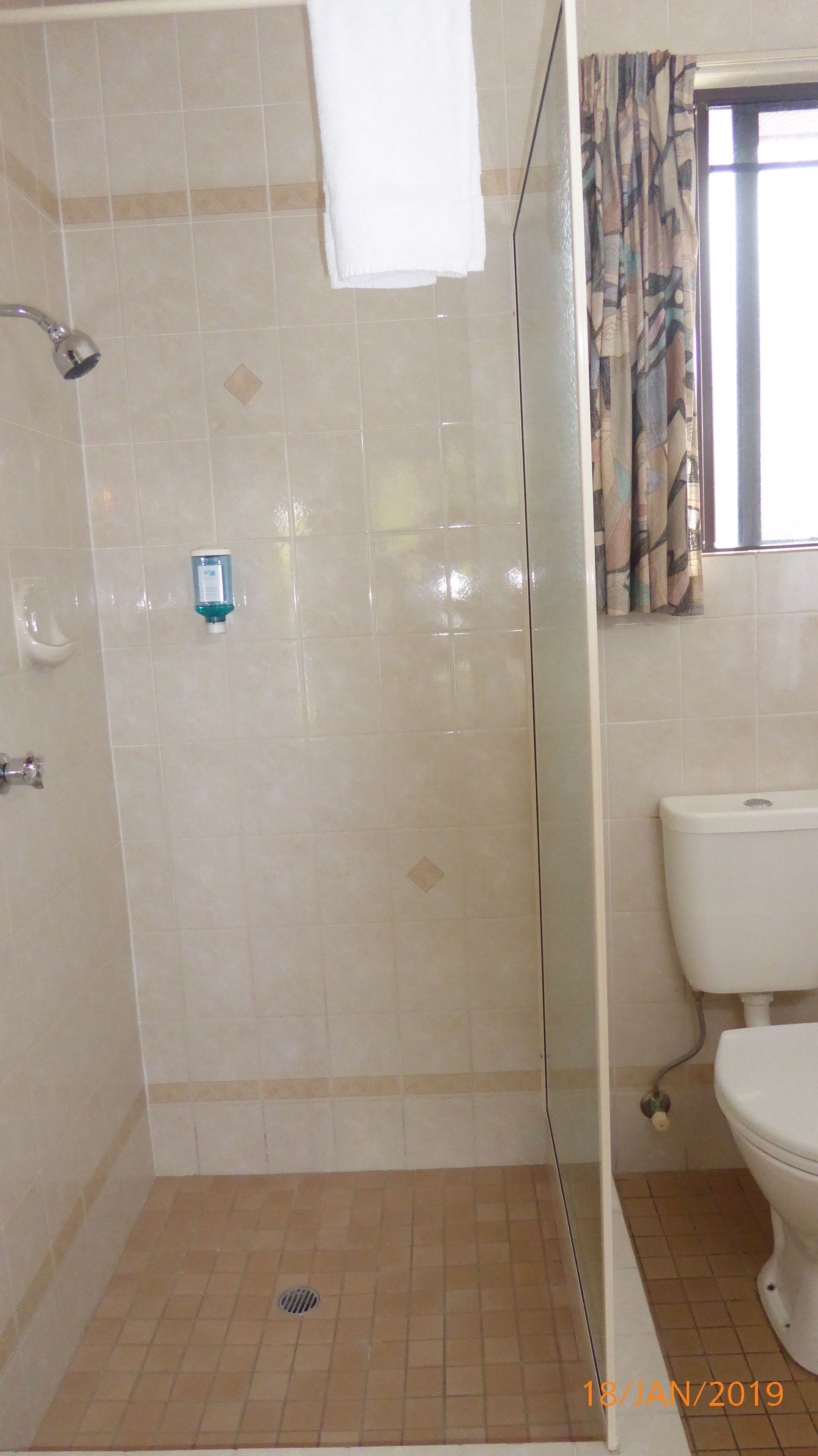 Un baño con ducha, inodoro y una ventana con cortinas.