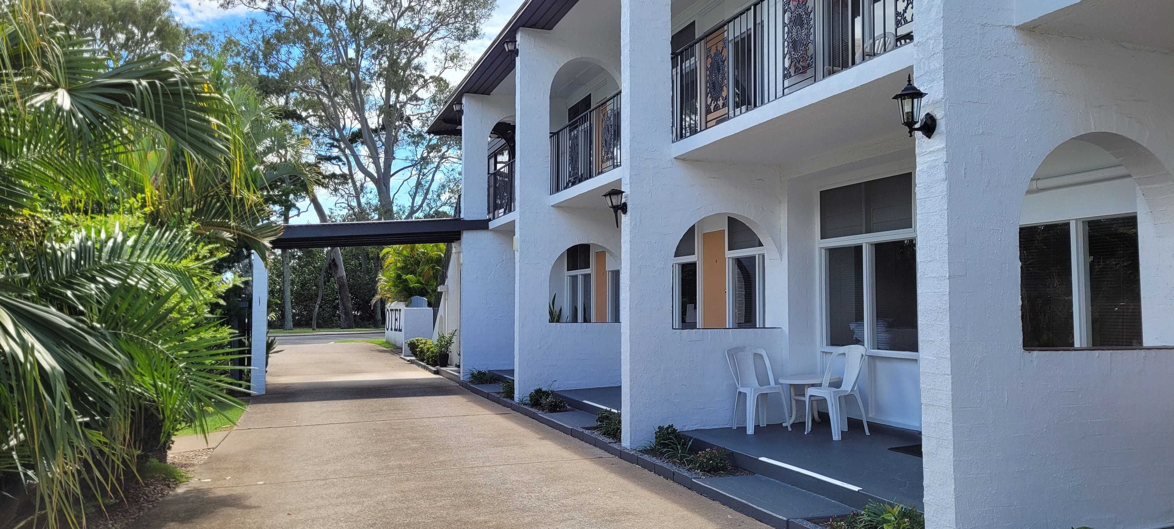 A two-story hotel with a covered walkway, outdoor seating, and a sign indicating it is a hotel.