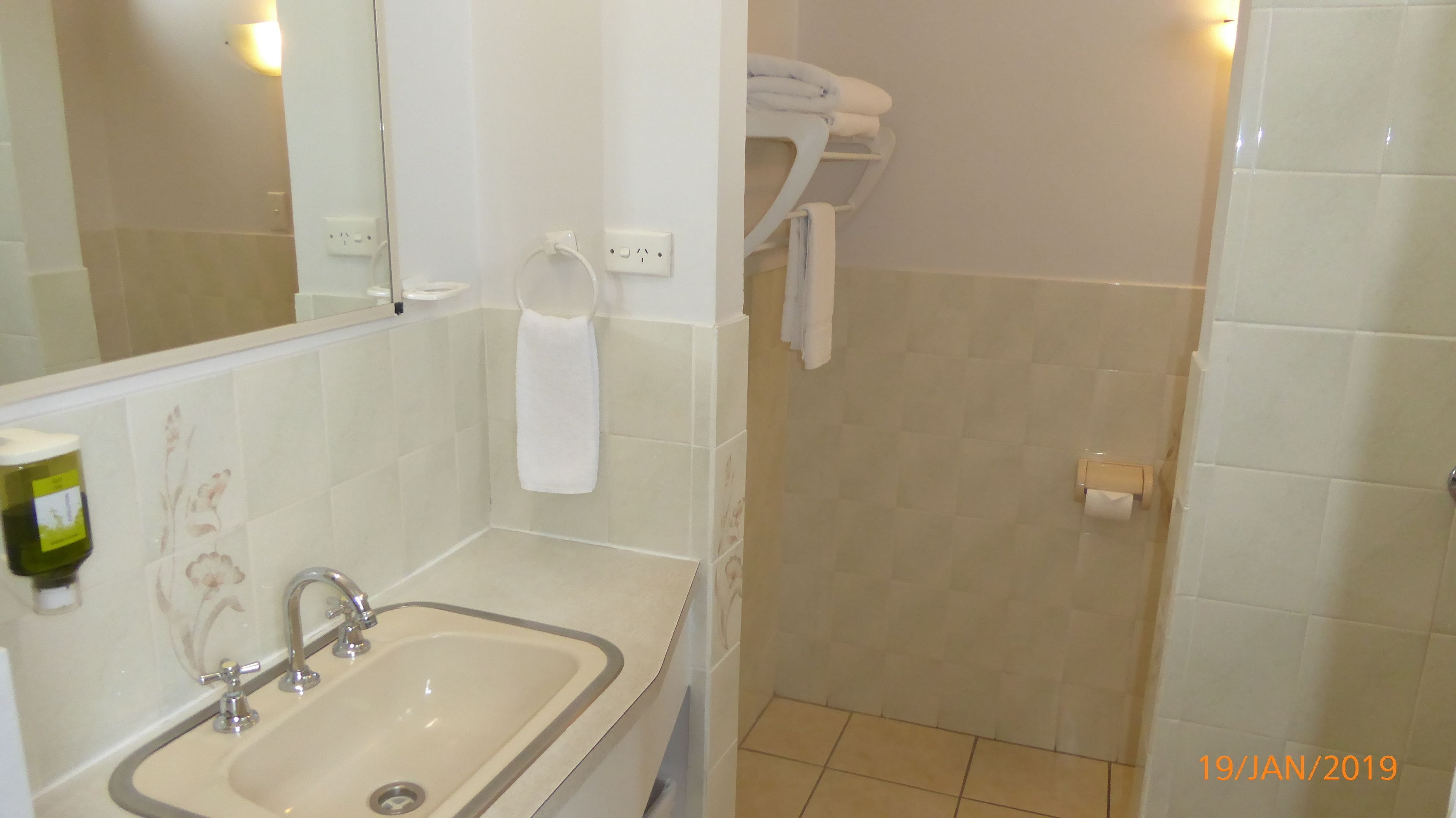 A bathroom with a sink, mirror, towel rack, and toilet paper holder.