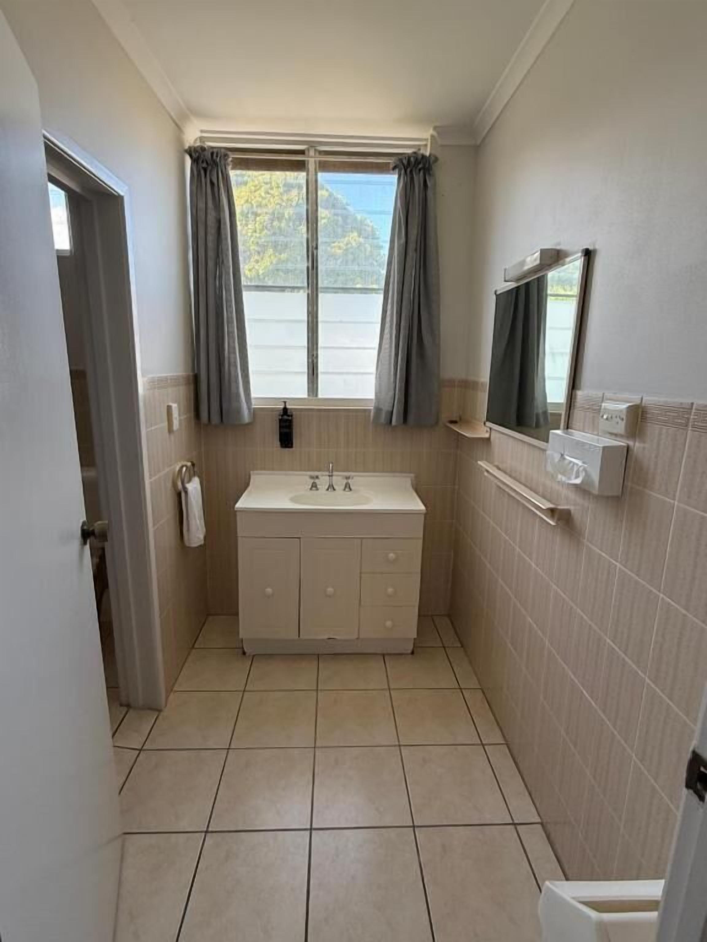Une salle de bain avec un lavabo, un miroir et une fenêtre avec des rideaux.