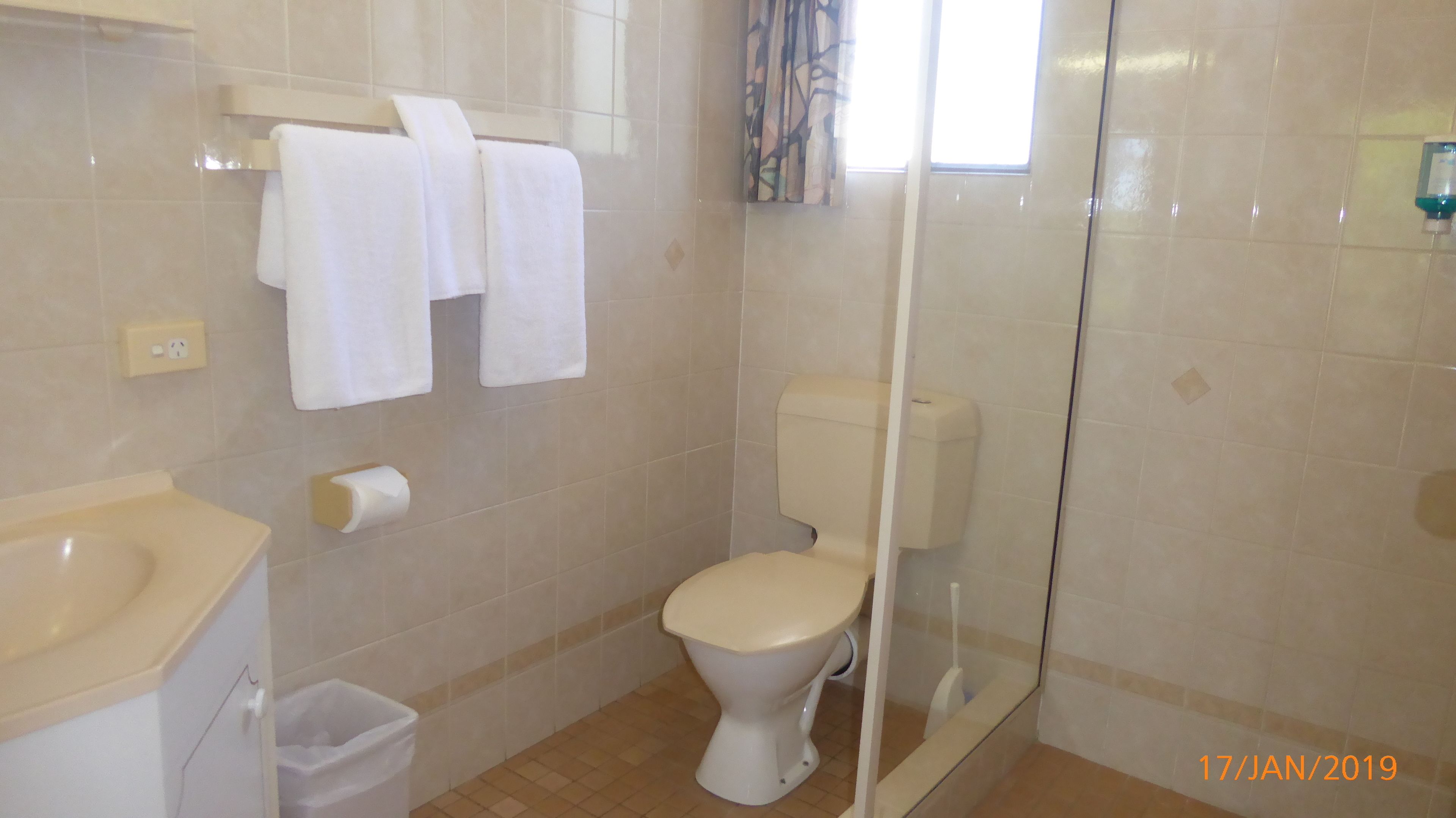 A bathroom with a toilet, a sink, a trash bin, and a shower area.