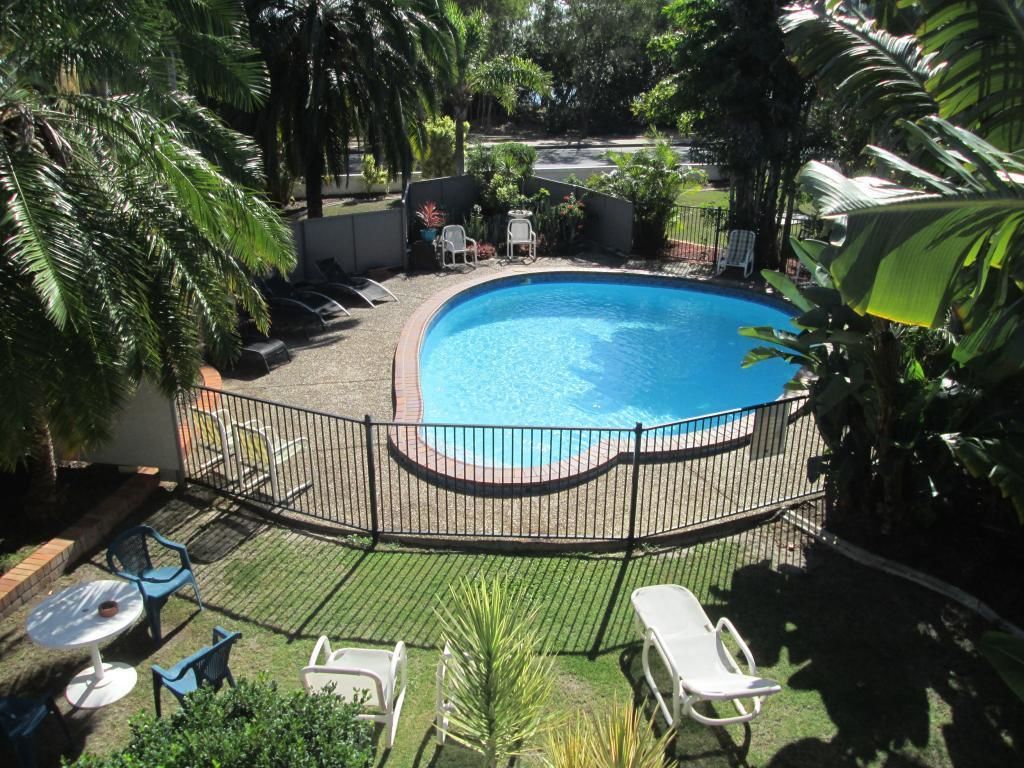 Una piscina rodeada por una valla, con sillas de descanso y una mesita cerca.
