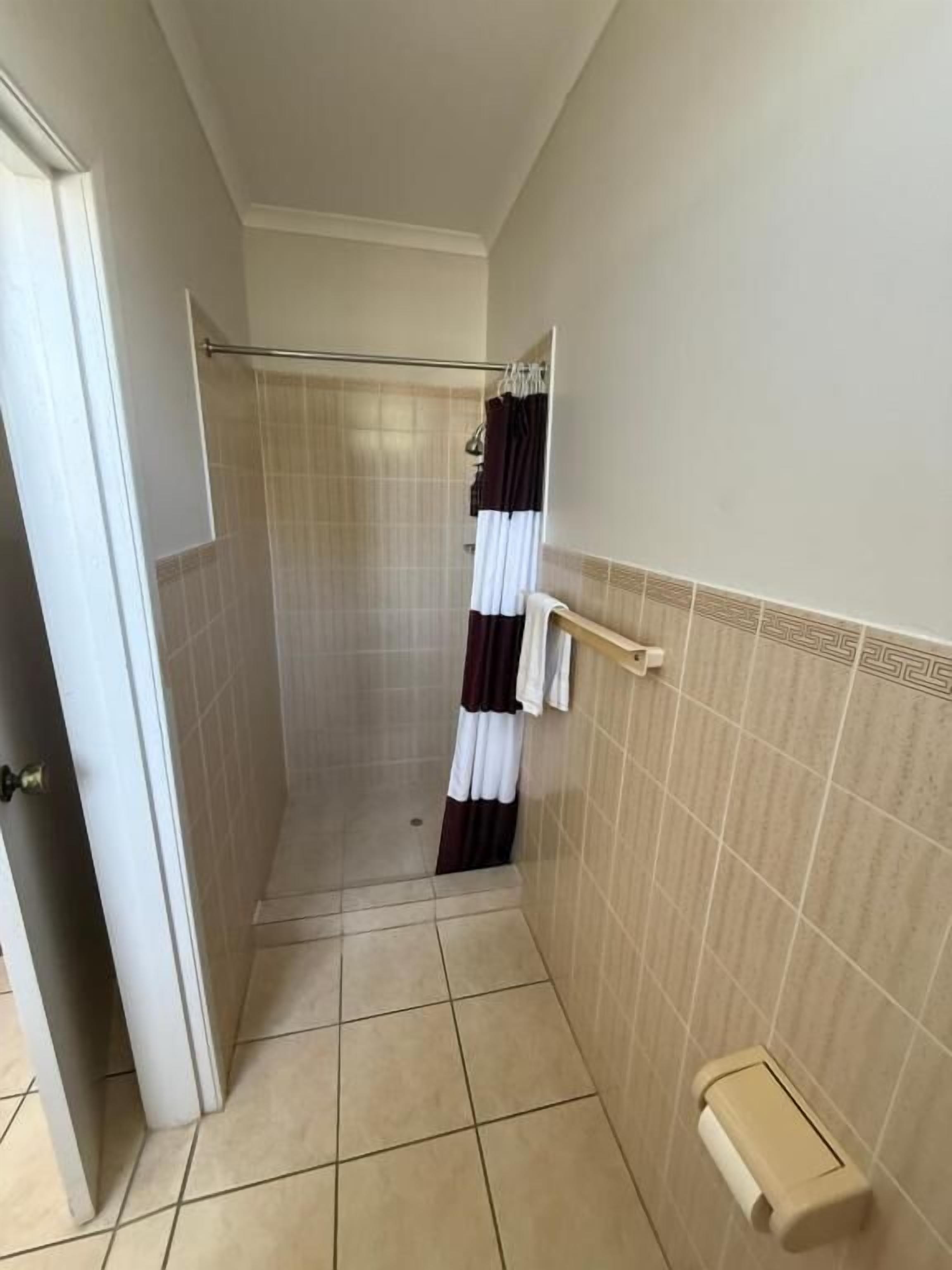 A narrow bathroom with a shower area, a towel rack, and a toilet paper holder.