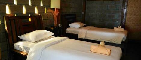 A hotel room with two beds, a wooden headboard, a nightstand, a lamp, and a brick wall.