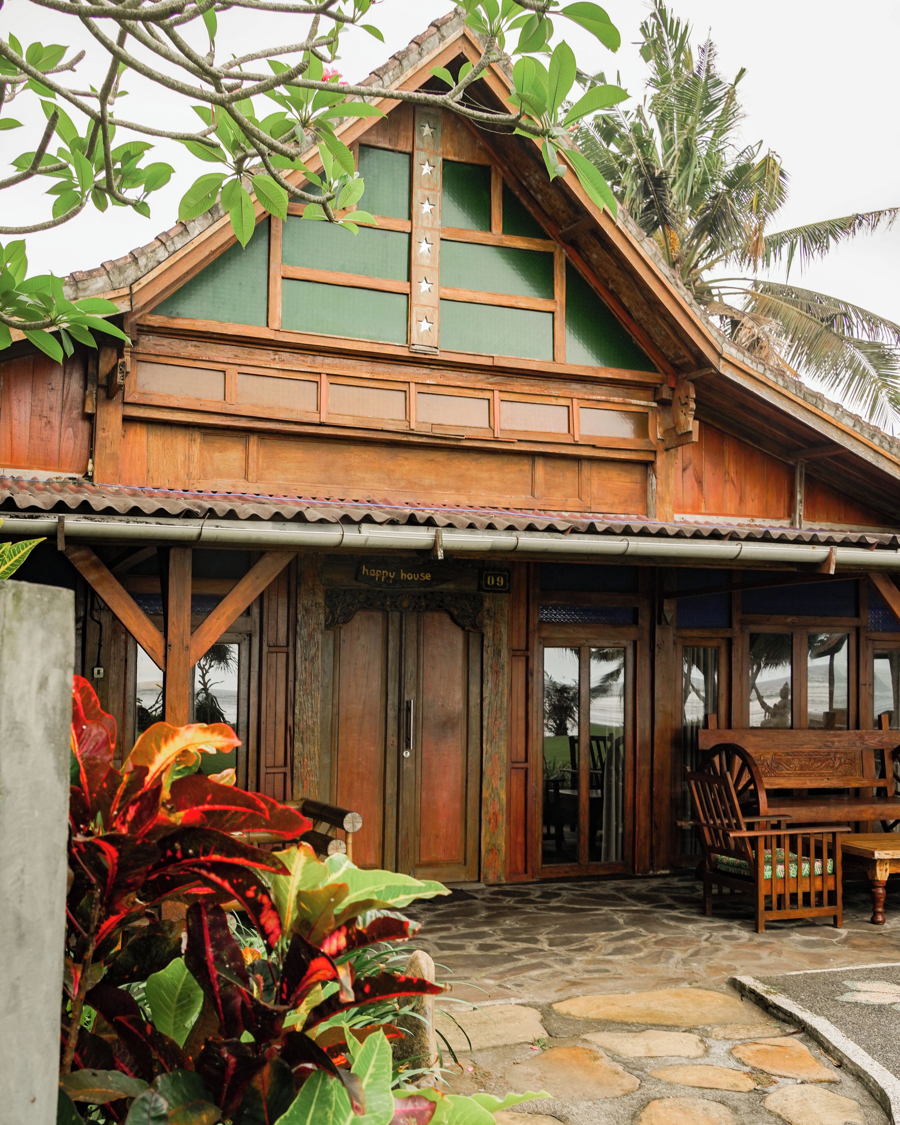 A wooden house with a green facade, a wooden porch, and a stone-paved entrance.