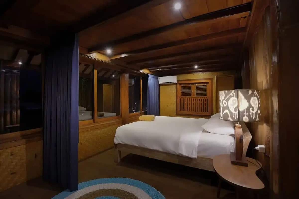 A wooden room with a bed, a lamp, and a window.