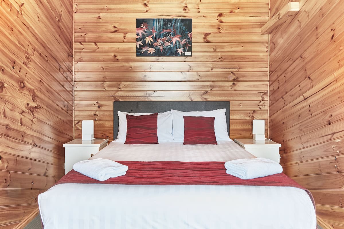 Una habitación con paneles de madera, una cama, dos mesitas de noche y un cuadro en la pared.