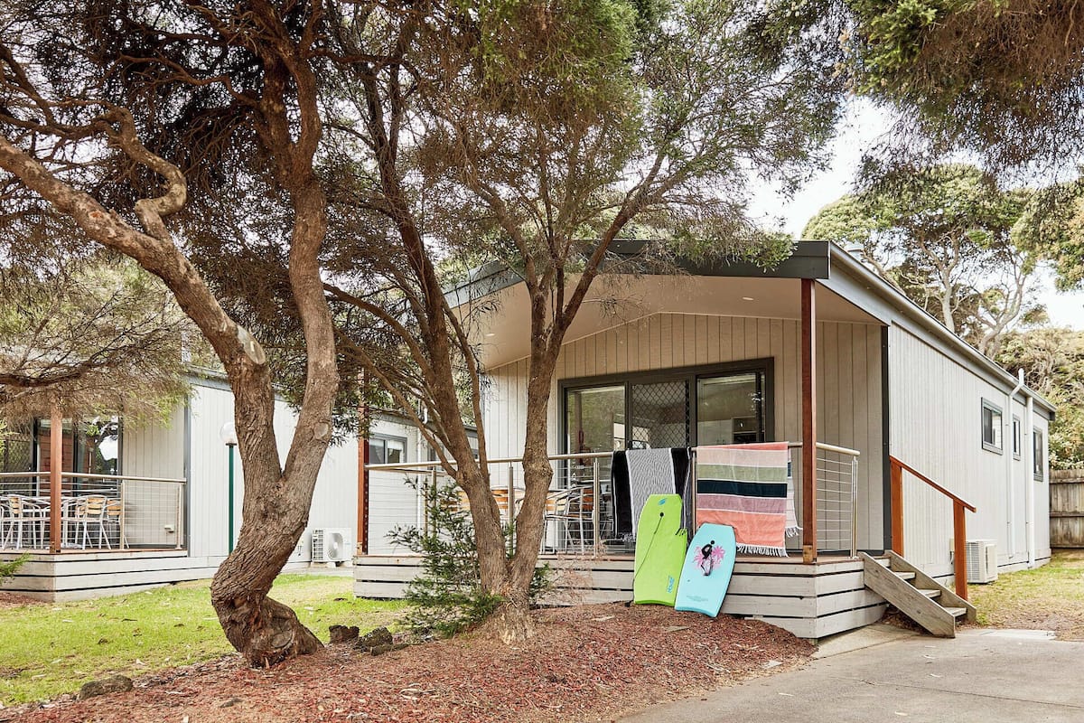 Una casa móvil de un piso con porche cubierto, un pequeño espacio de exterior con mobiliario y una escalera que lleva a la entrada.