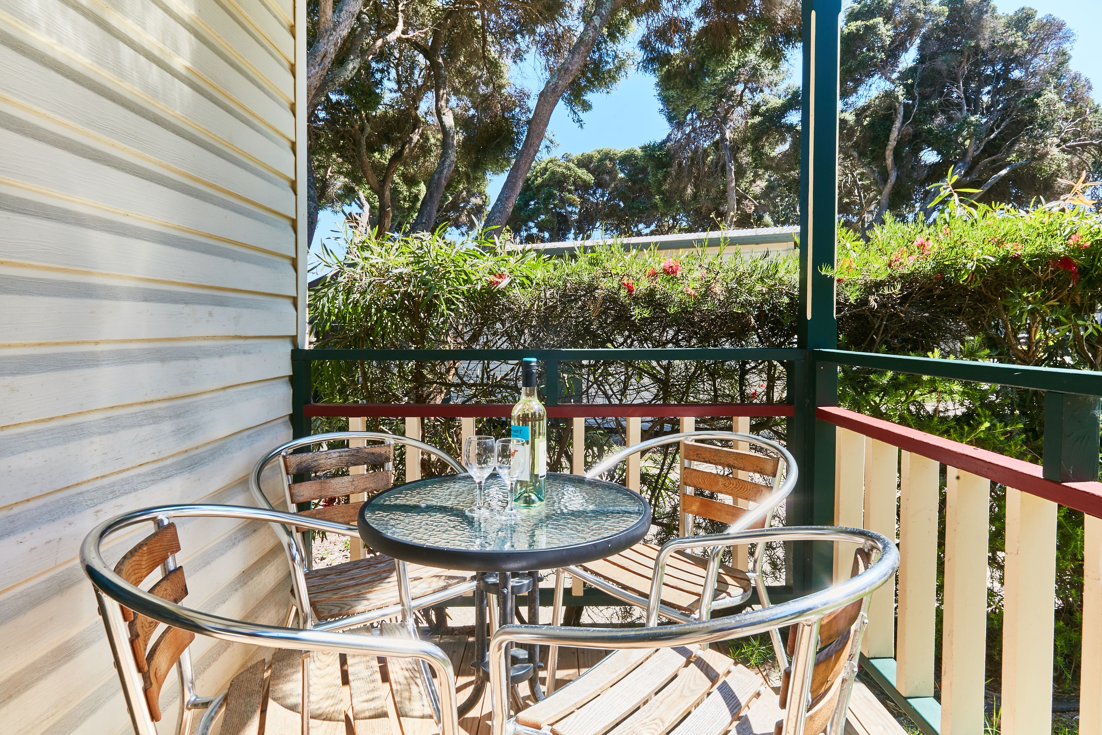 A round table with four chairs on a balcony with a view of trees.