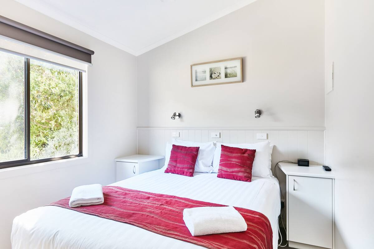 Habitación de hotel con una cama grande, una mesita de noche, un armario pequeño y una ventana con vistas a zonas verdes.