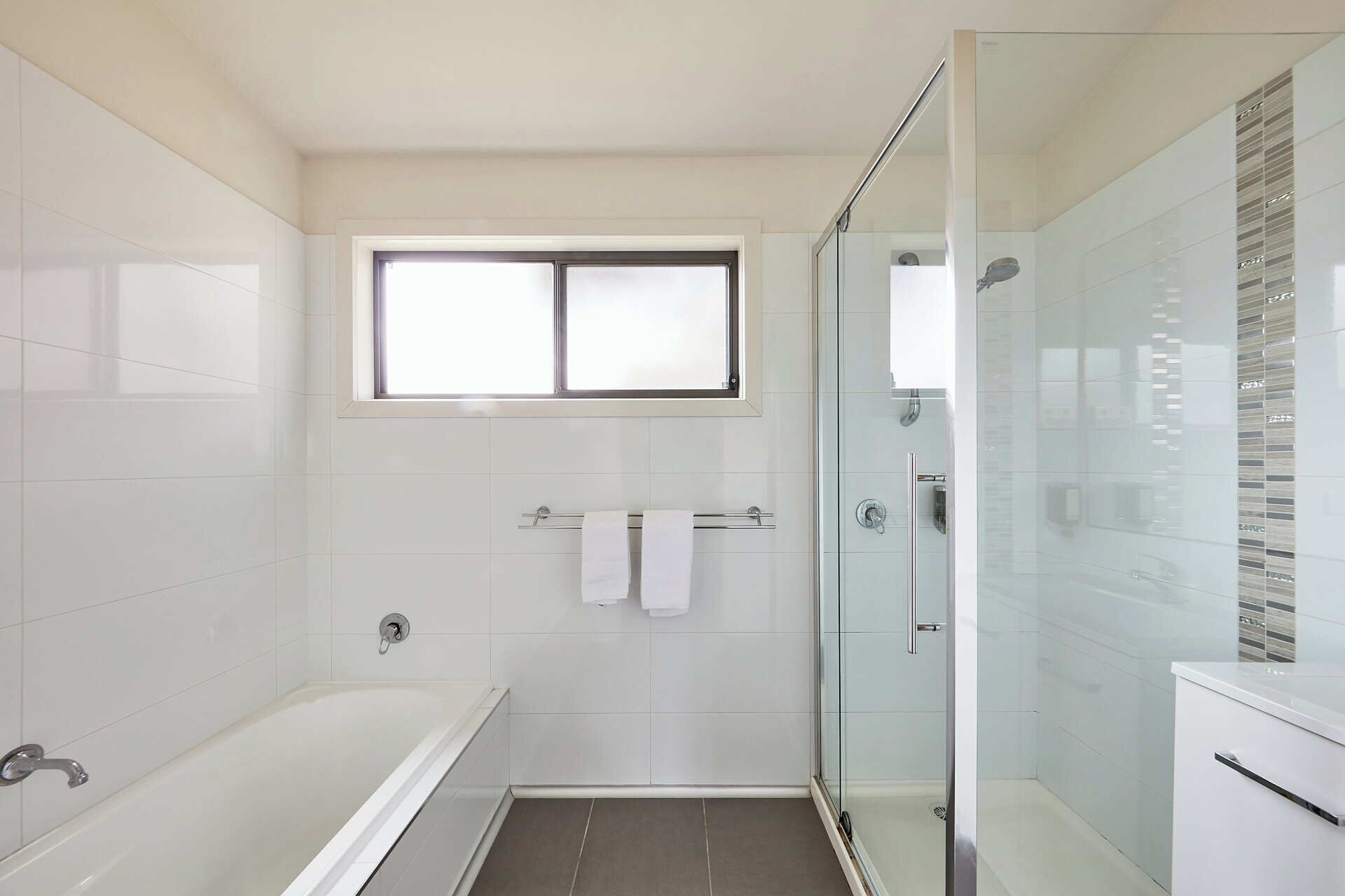 Un baño moderno con bañera, ducha con mampara de vidrio y ventana sobre el lavamanos.