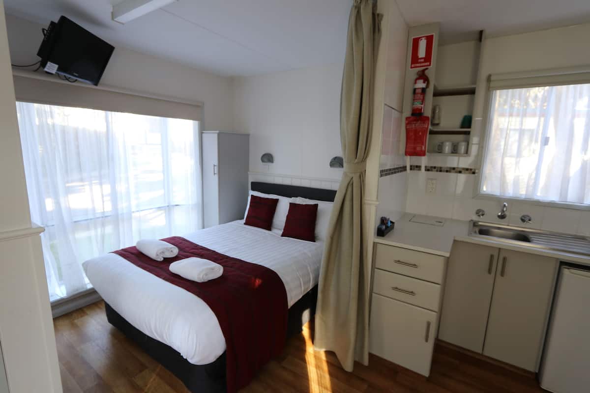 Habitación de hotel con cama, ventana con cortinas, kitchenette y televisor montado en la pared.