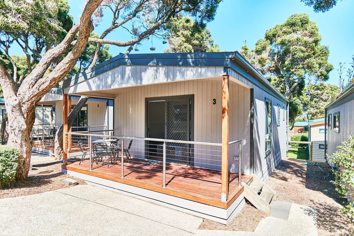 Una cabaña moderna de un solo nivel, con terraza de madera y zona exterior cercada.