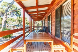 A wooden deck with a table and benches, overlooking a parking area and trees.